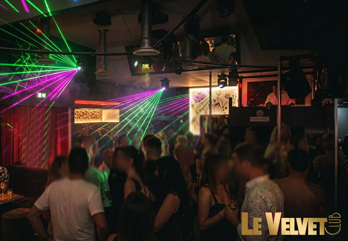 Une piste du Velvet Club pleine de danseurs sous des faisceaux laser verts et violets, la cabine du DJ en fond