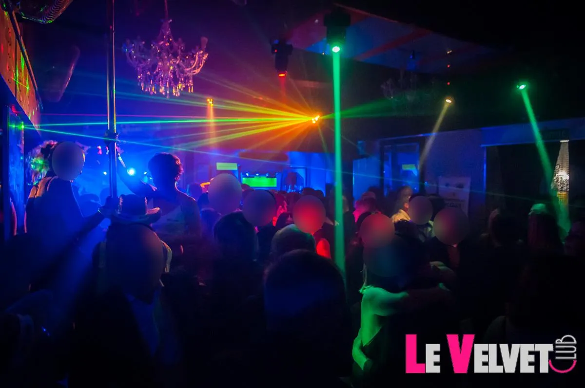 Une soirée au Velvet Club : la foule danse sous les lasers et un lustre, une barre de pole dance au centre de la piste